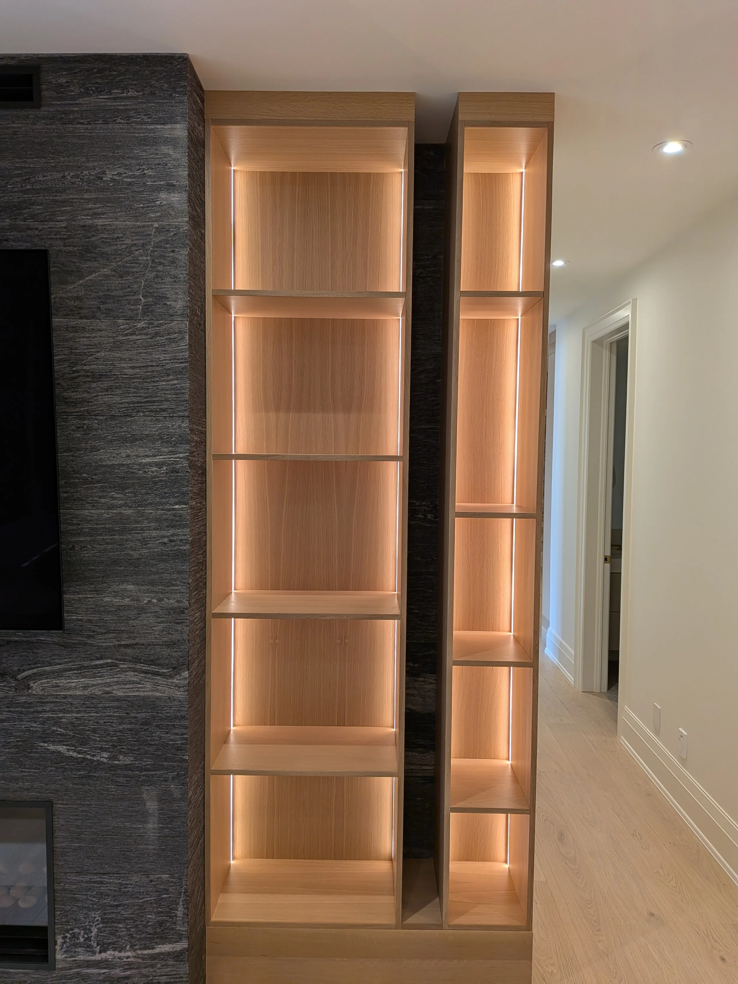 Empty wooden bookshelf with LED lighting, situated in a modern interior with hardwood flooring and white walls.