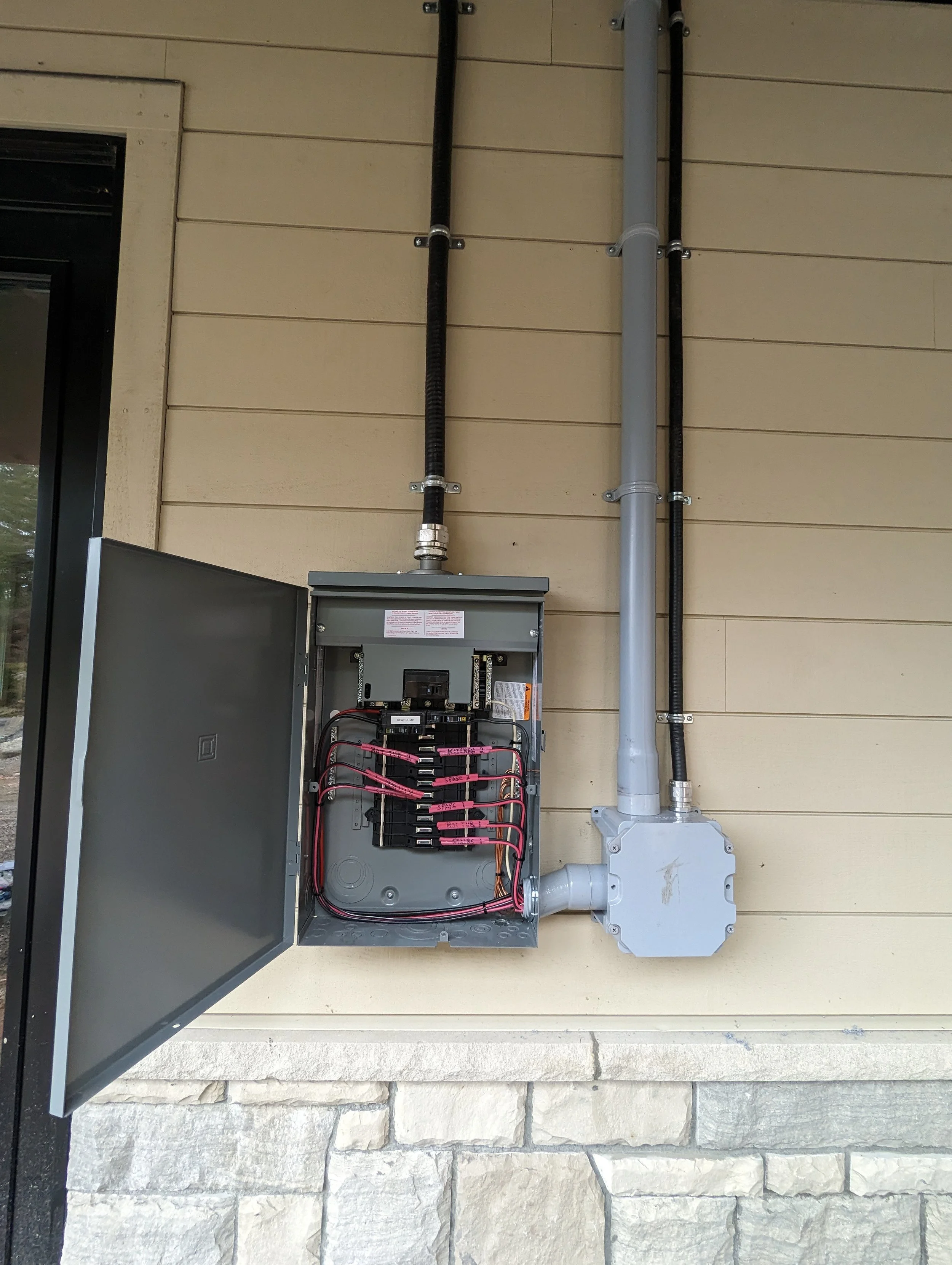 Electrical meter box and electrical conduit pipes on the exterior wall of a building.