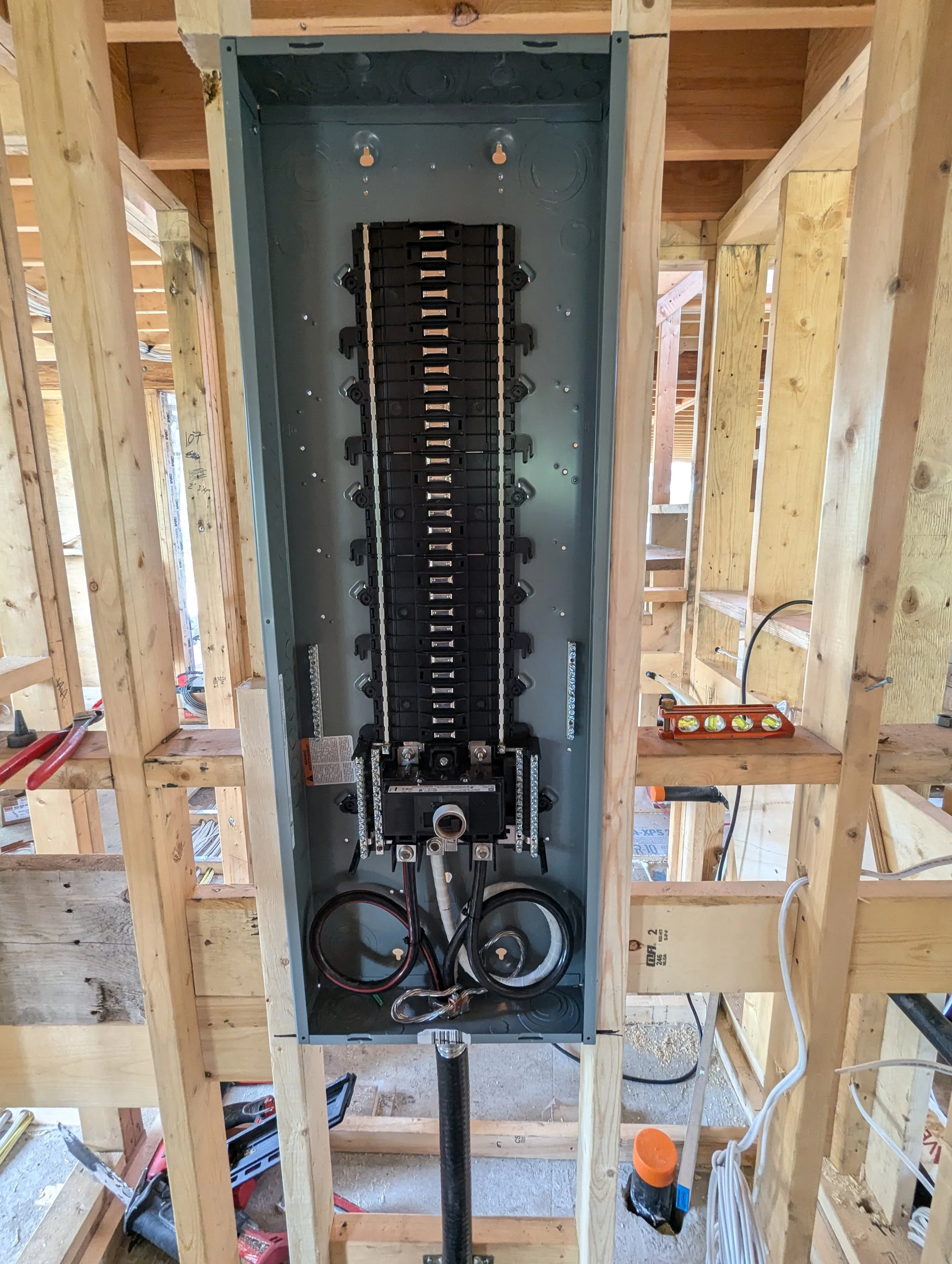 Electric panel being installed in a wooden wall framing at a construction site.