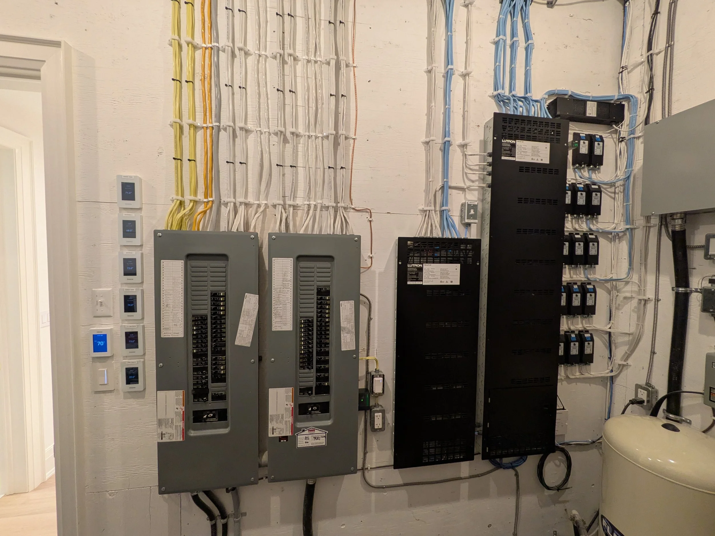 Electrical panels with circuit breakers and wiring on a wall, Luton homework's lighting panels on the right and various electrical components next to them.