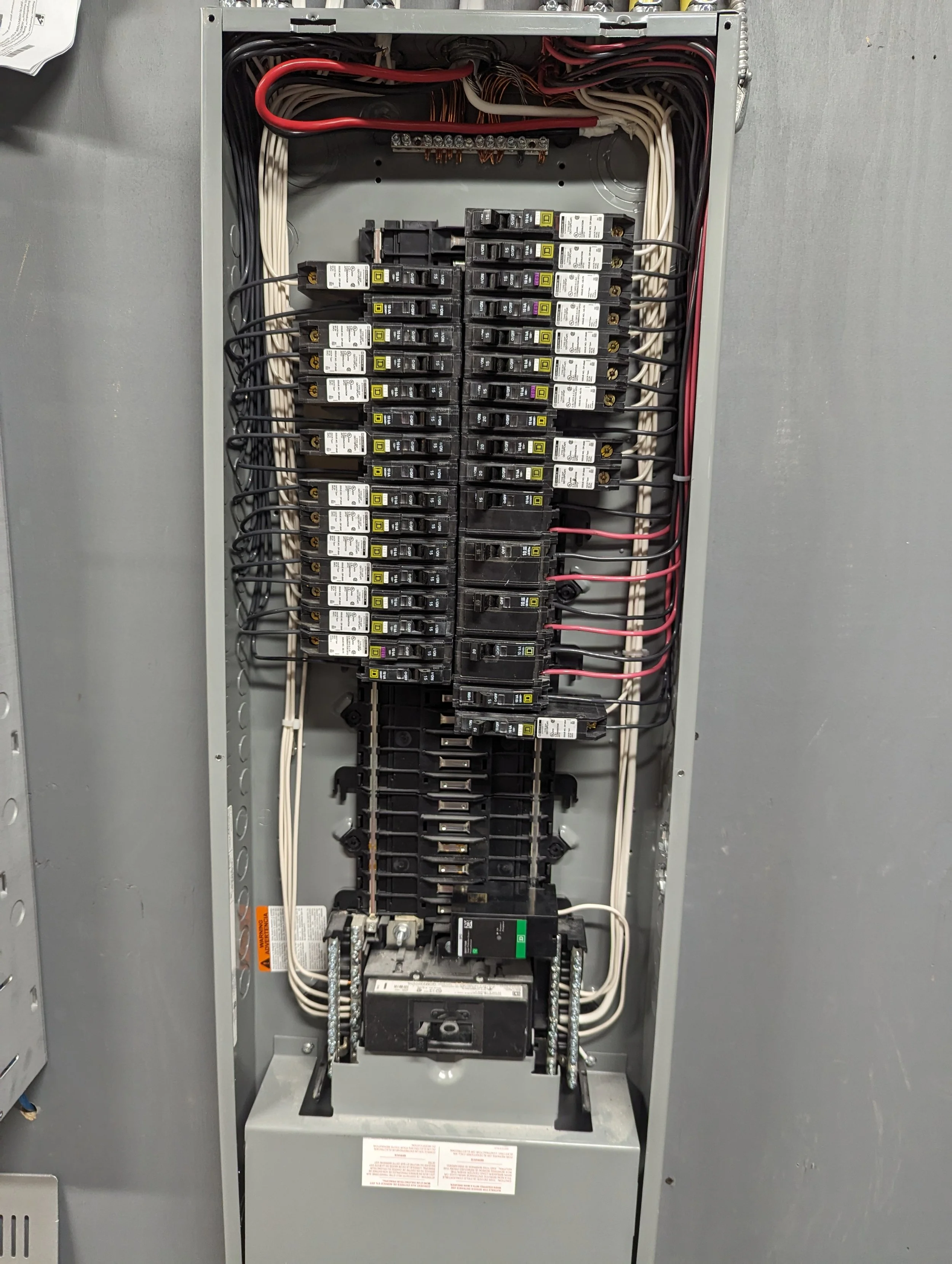 An electrical breaker panel with multiple switches and wires inside a gray metal enclosure.