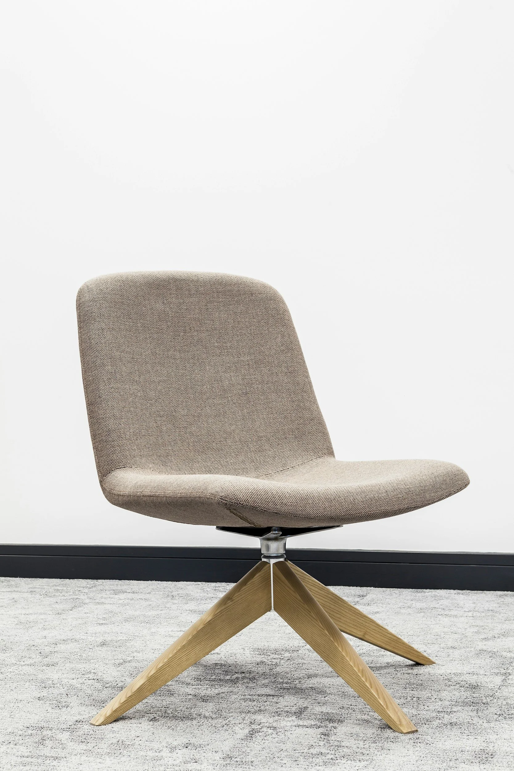 A beige modern office chair on a grey carpet against a white wall.