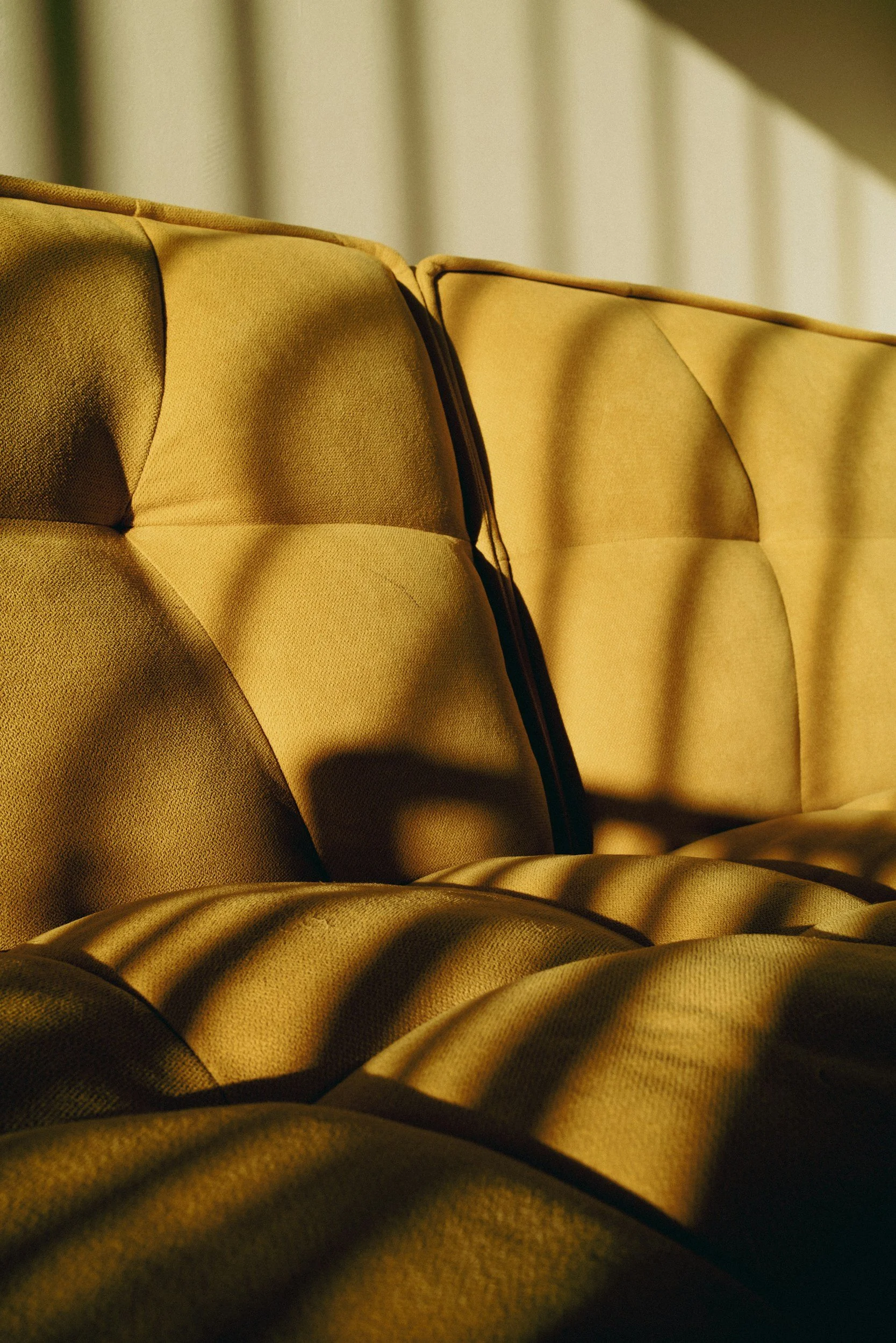 Close-up of a yellow upholstered sofa with tufted cushions and shadows.
