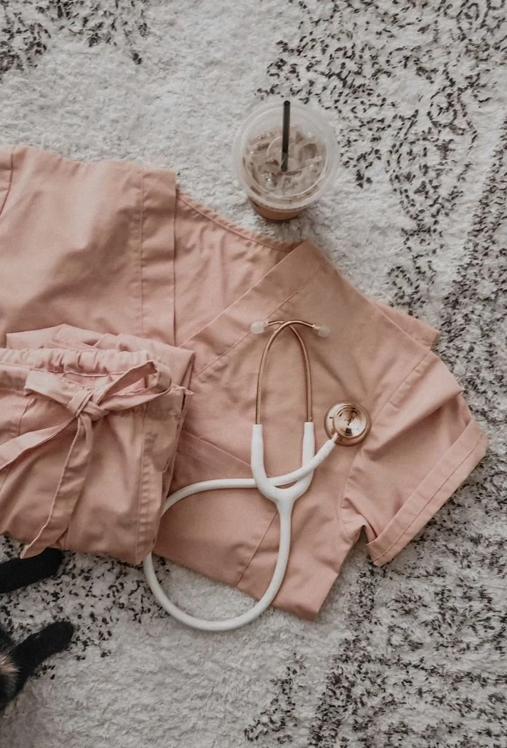 Pink medical scrubs, a stethoscope, and a plastic cup with iced coffee on a rug.