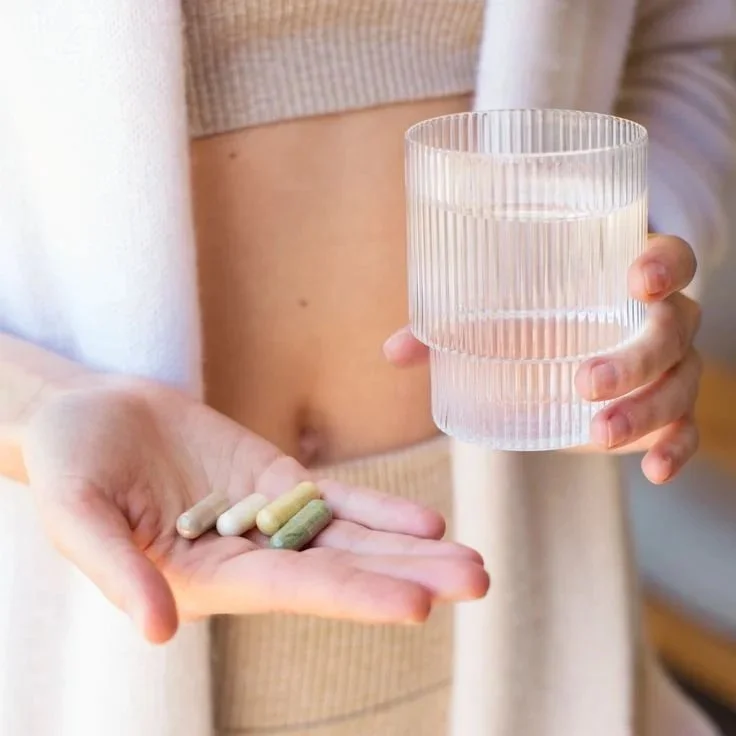 A person holding a glass of water in one hand and several pills in the other hand.