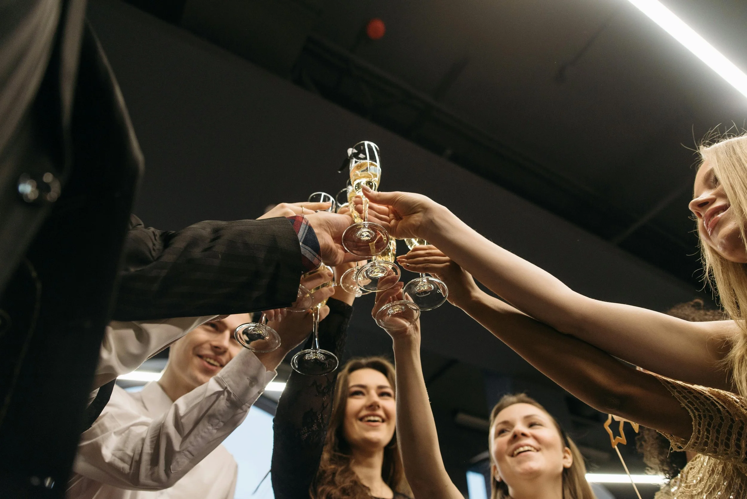 Bir grup insan el ele tutuşarak kadeh tokuşturuyor, mutlu ve gülümseyen yüzlerle kutlama yapıyorlar.