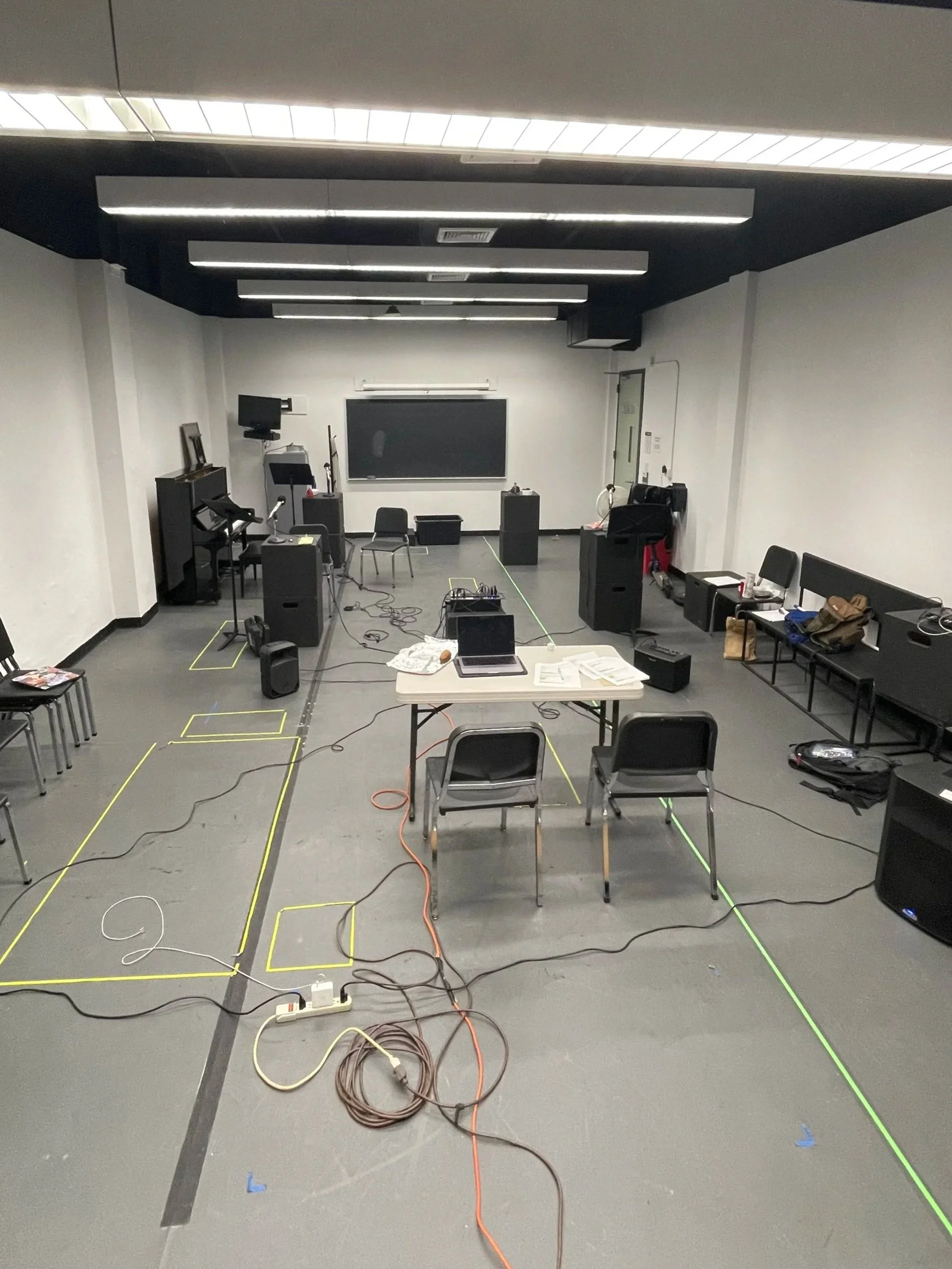 Empty classroom or lecture hall with chairs, tables, and equipment set up for filming or testing, marked with lines and tape on the floor.