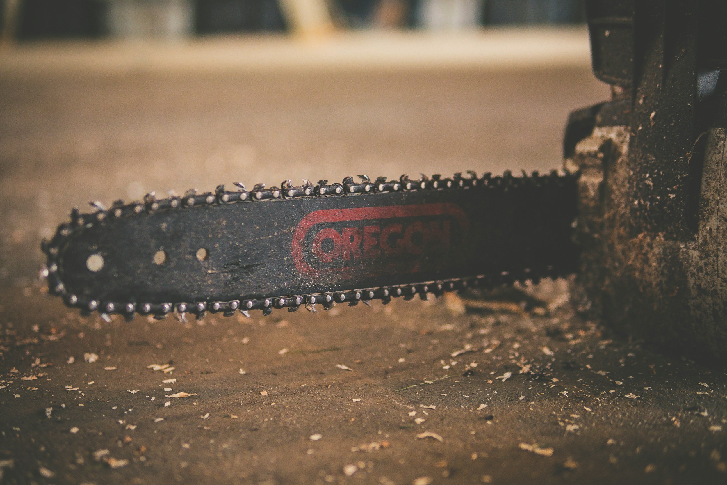 Close-up of a chainsaw chain with the brand name Oregon visible, resting on a muddy surface.