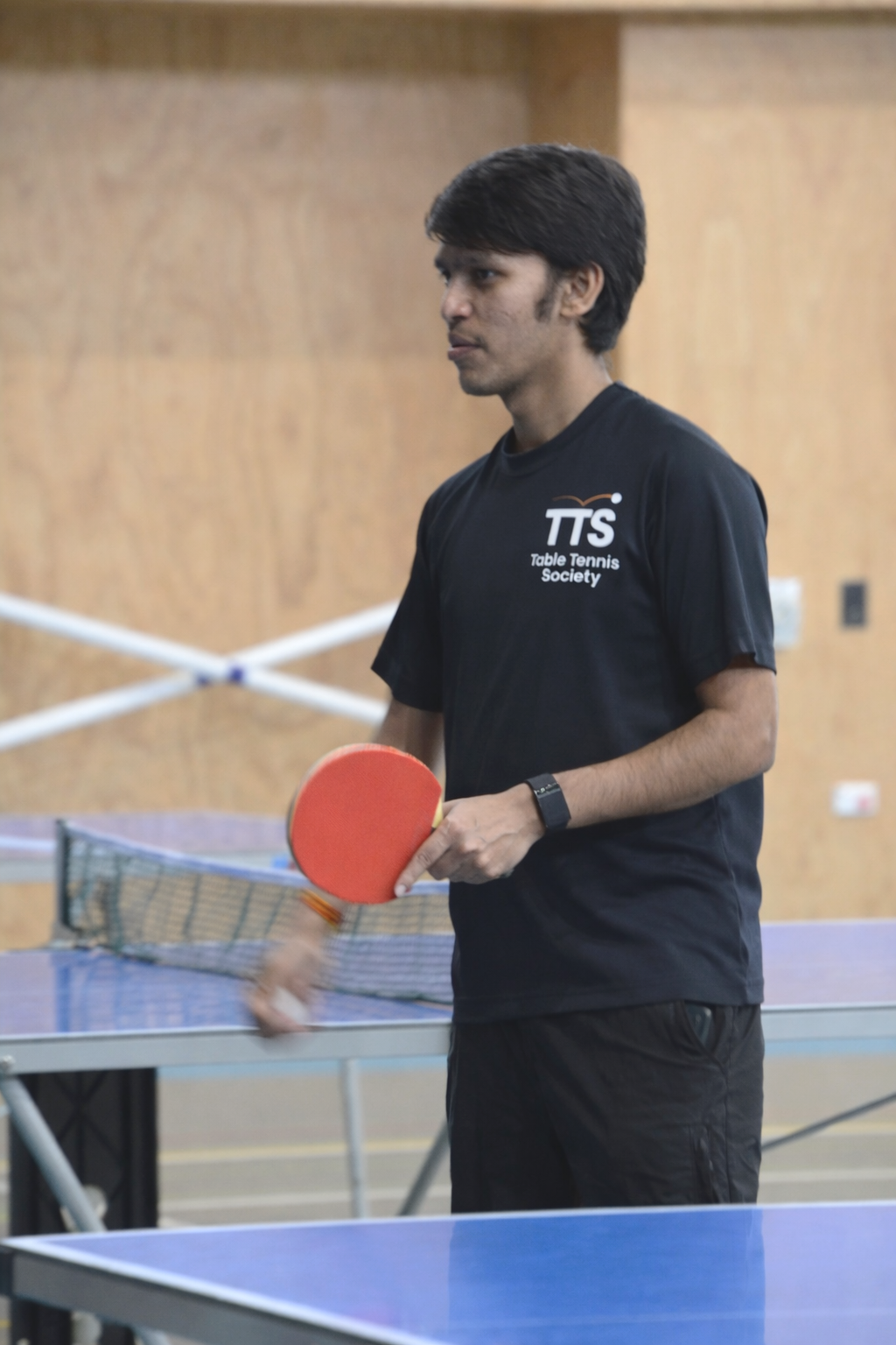 Male coach with table tennis or ping pong bat in hand speaking to students.