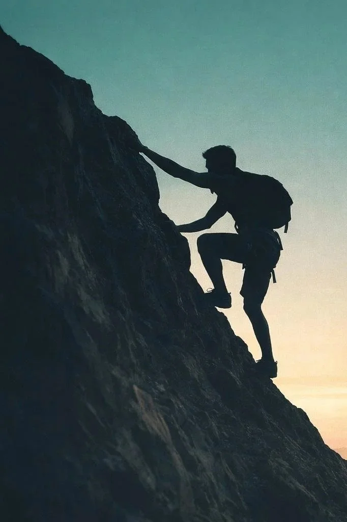 Silhouette of a person climbing a steep rocky cliff at sunset.
