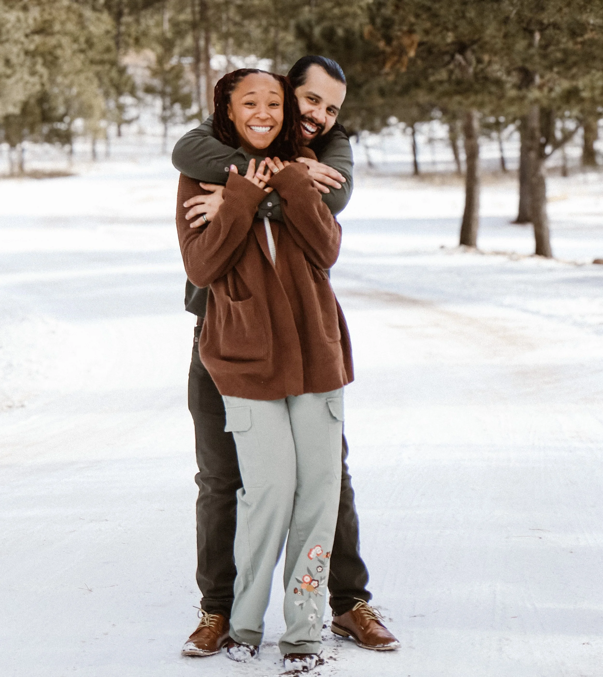 A happy couple outdoors in a snowy park, hugging and smiling at the camera.