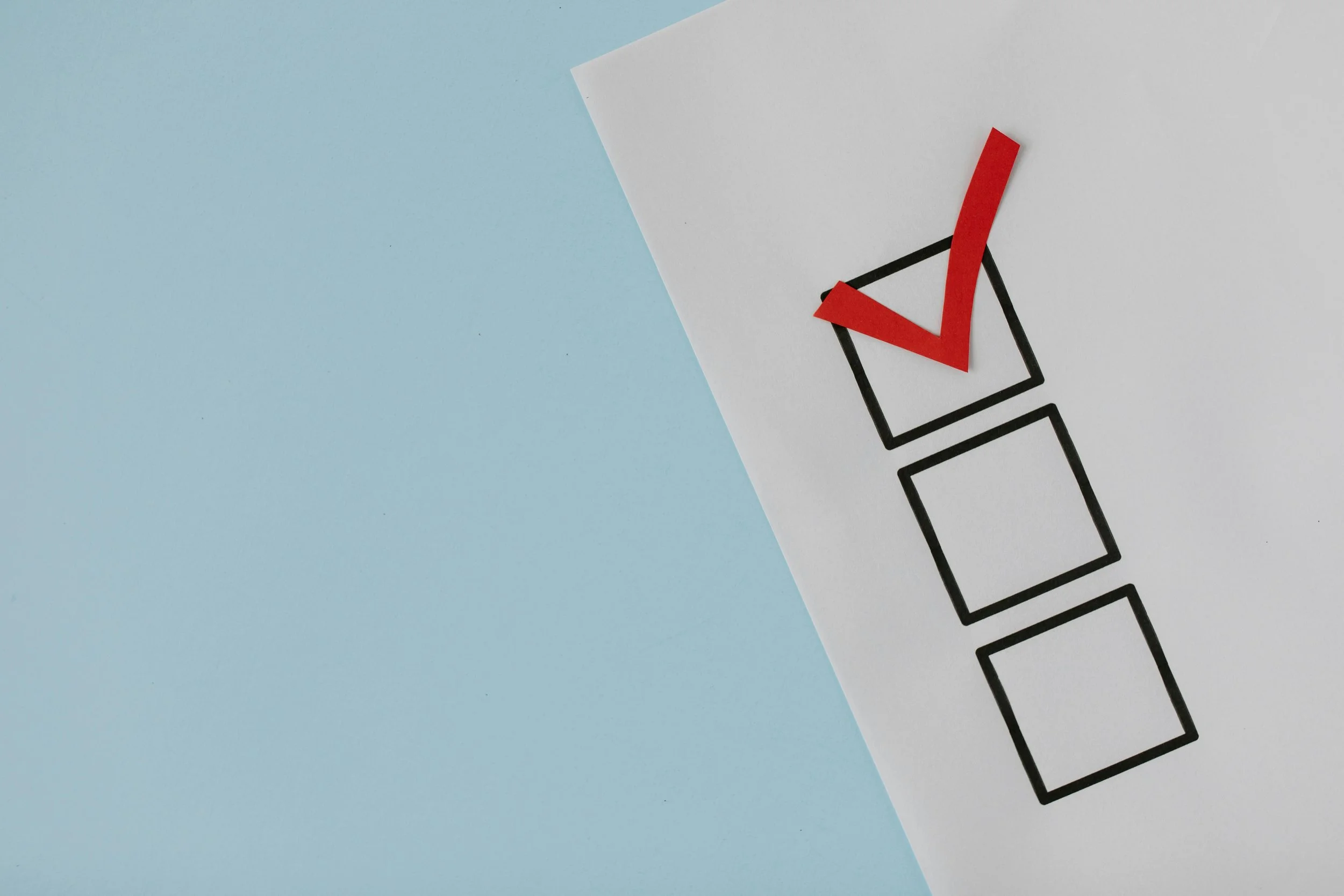 A checklist with three empty boxes on white paper, one box marked with a red check, on a surface with a blue background.