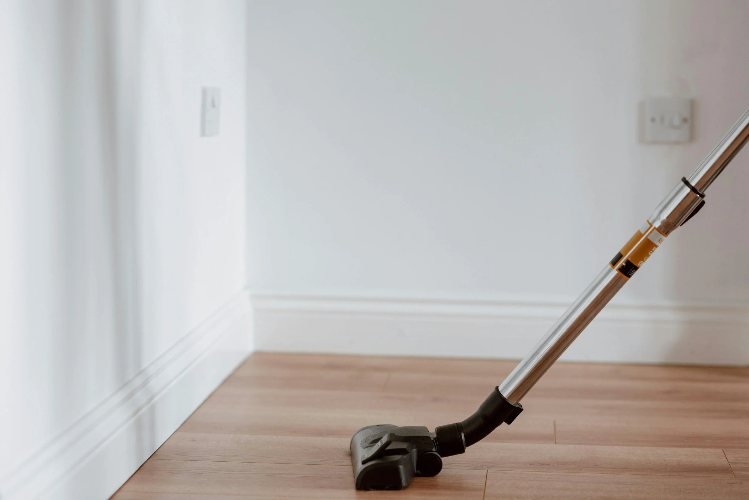 Vacuum cleaner on a wooden floor near a white wall with electrical outlets.
