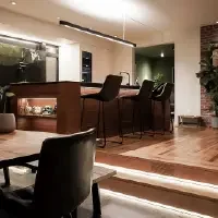 Modern kitchen and dining area with wooden flooring, bar stools at a kitchen island, indoor plants, and decorative items on the table.