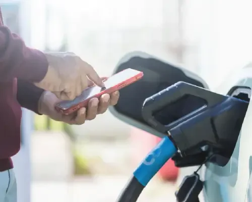 Image of an EV plugged in and charging while the car owner accesses their smartphone to monitor the charging status.
