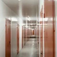 A long, narrow corridor with multiple orange doors and fluorescent ceiling lights.