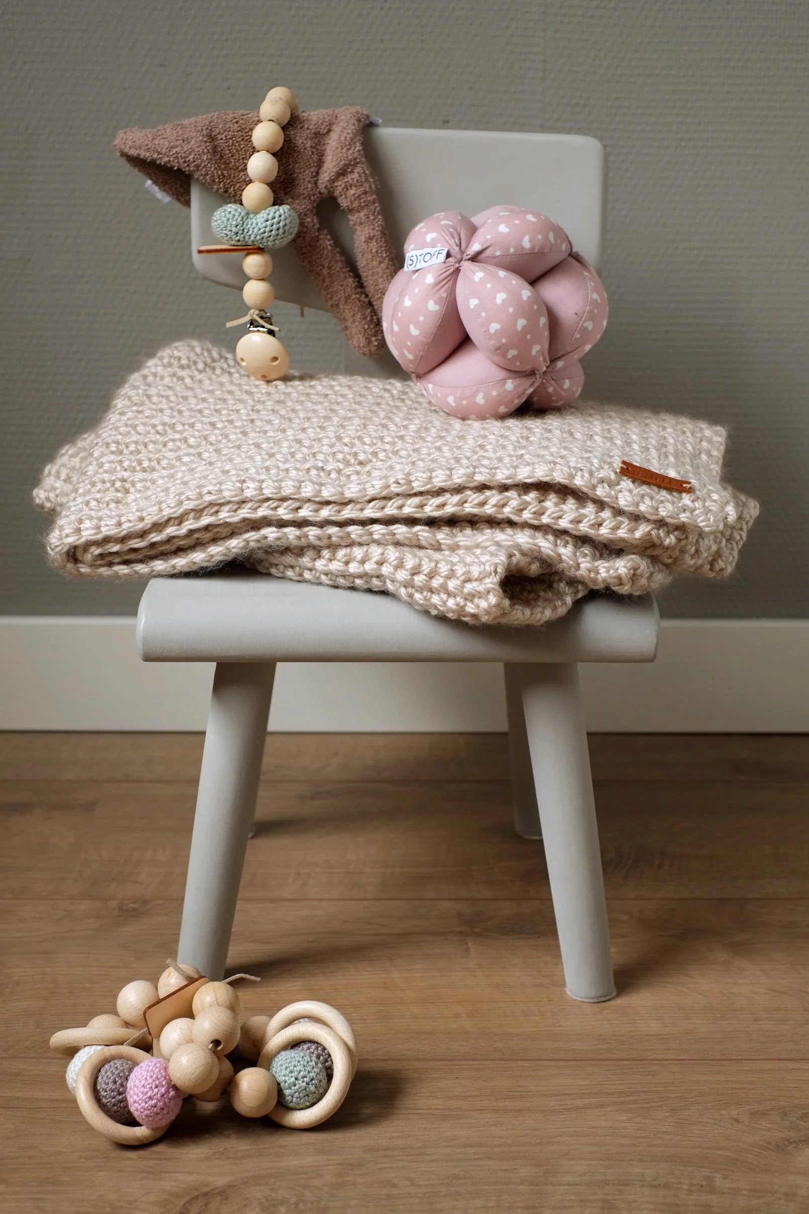 Babypoppen en accessoires op een kinderstoel, inclusief een knuffel, deken, en houten bijtspeelgoed.