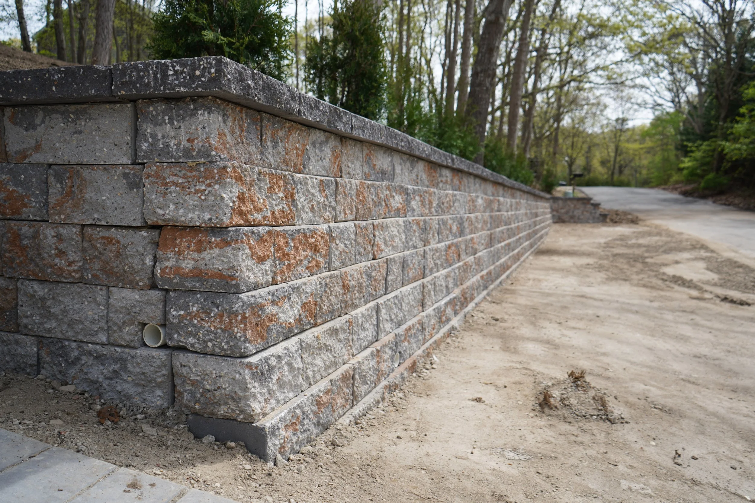 A stone retaining wall beside a dirt pathway in a wooded area.