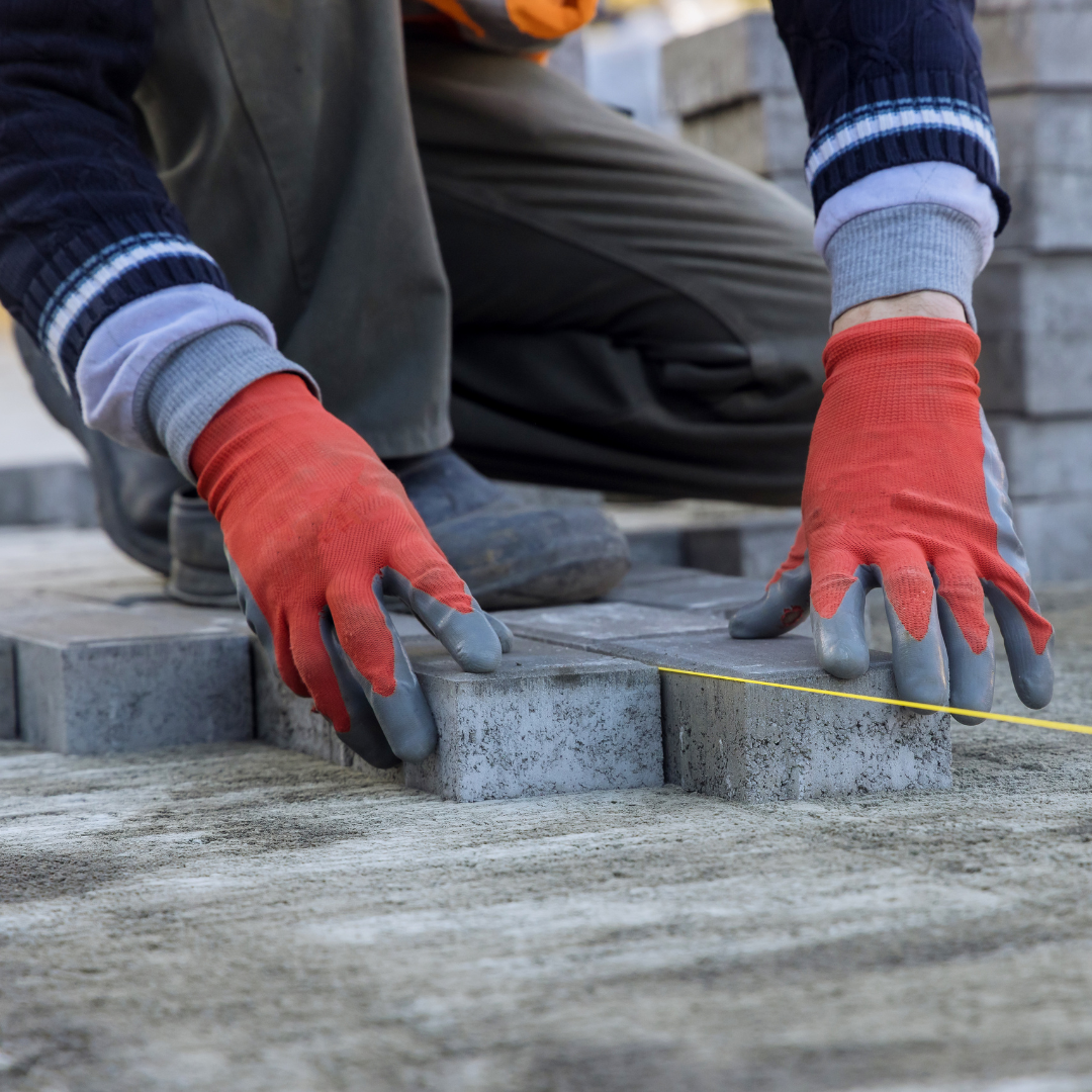 Worker laying concrete blocks on a foundation, using a measuring tape for alignment