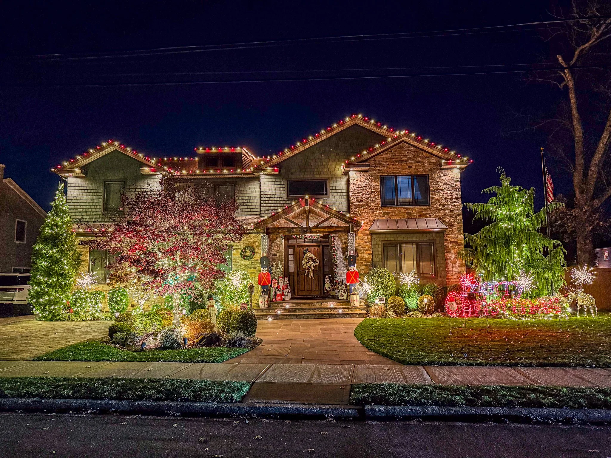 Decorated house with Christmas lights, nutcracker and Santa Claus figurines, a Christmas tree, and illuminated deer and snowflakes outside at night.