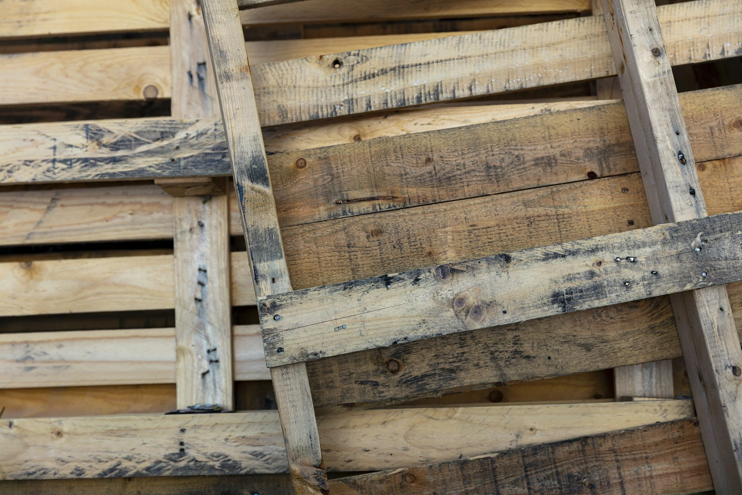 Stacked wooden pallets, some weathered and darkened, with visible nails and grain patterns.