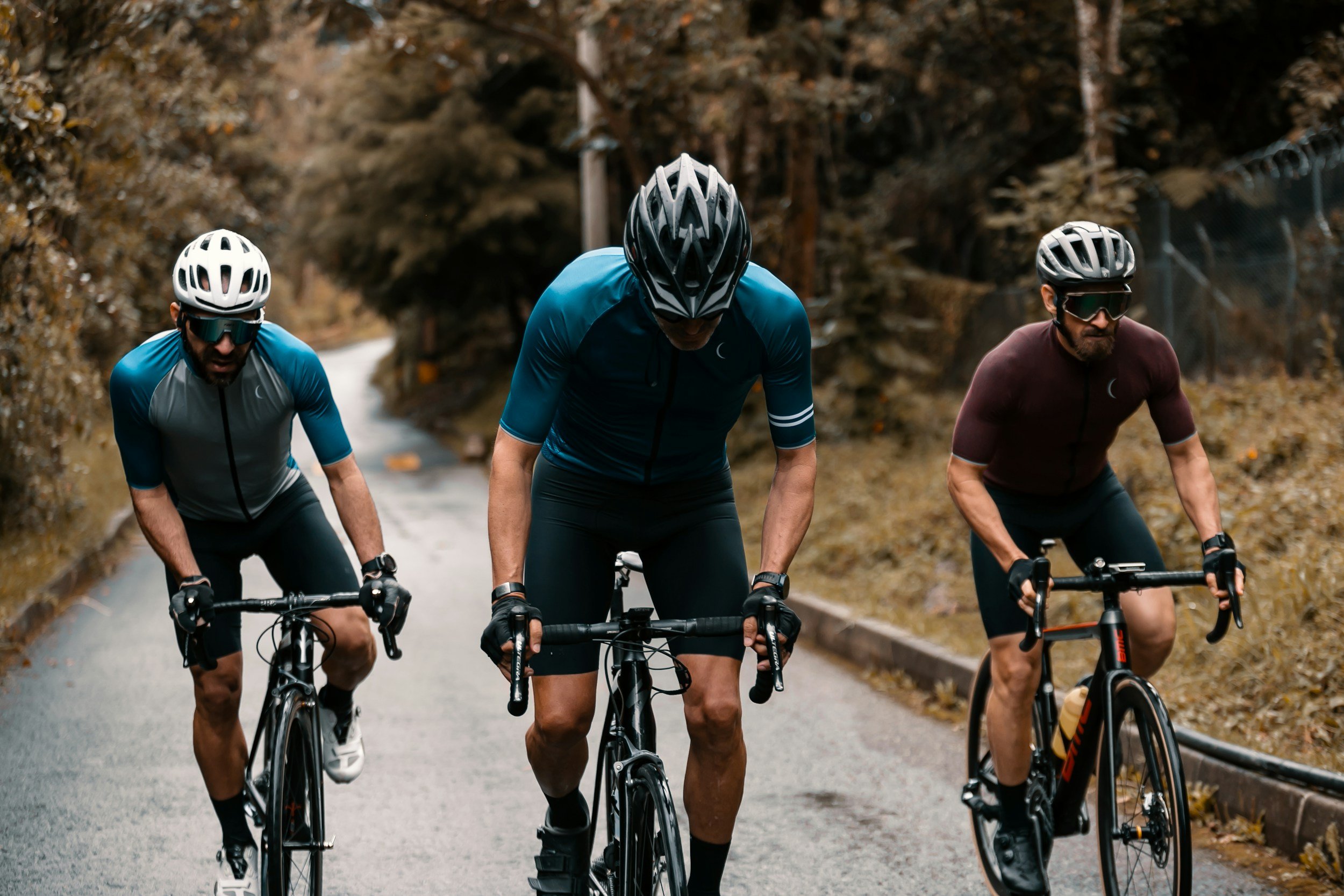 Three male cyclists riding mountain bikes on a wet, forested road in an overcast setting.
