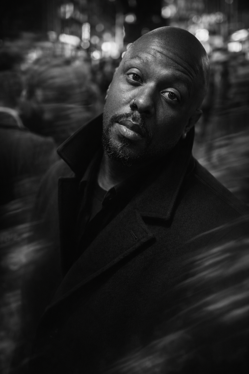 Close-up black and white portrait of a bald man with a beard and mustache, wearing a jacket, looking directly at the camera with a confident expression.