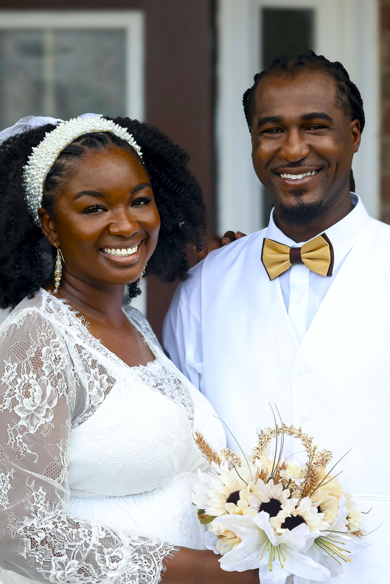 A smiling bride and groom at their wedding, with the bride holding a bouquet of sunflowers and white flowers.