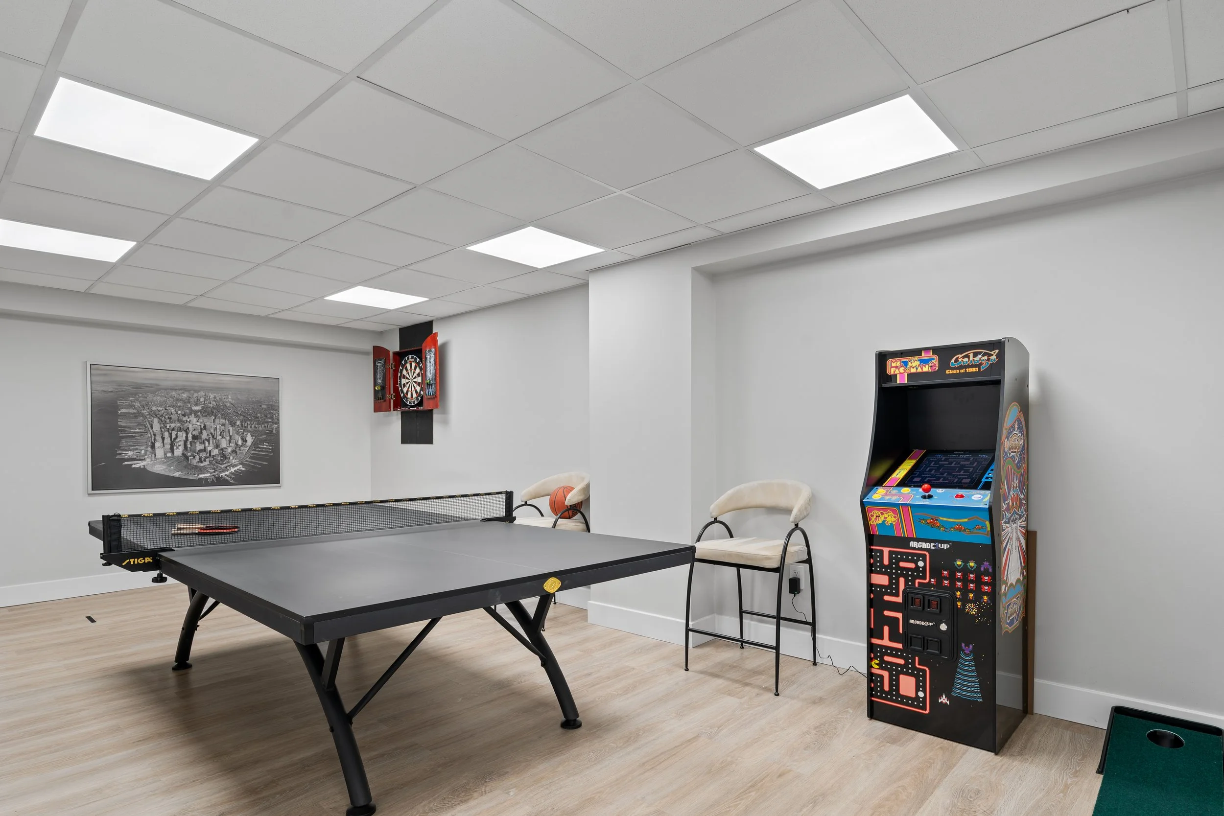 Game room with ping pong table, arcade machine, dartboard, chairs, and wall art.