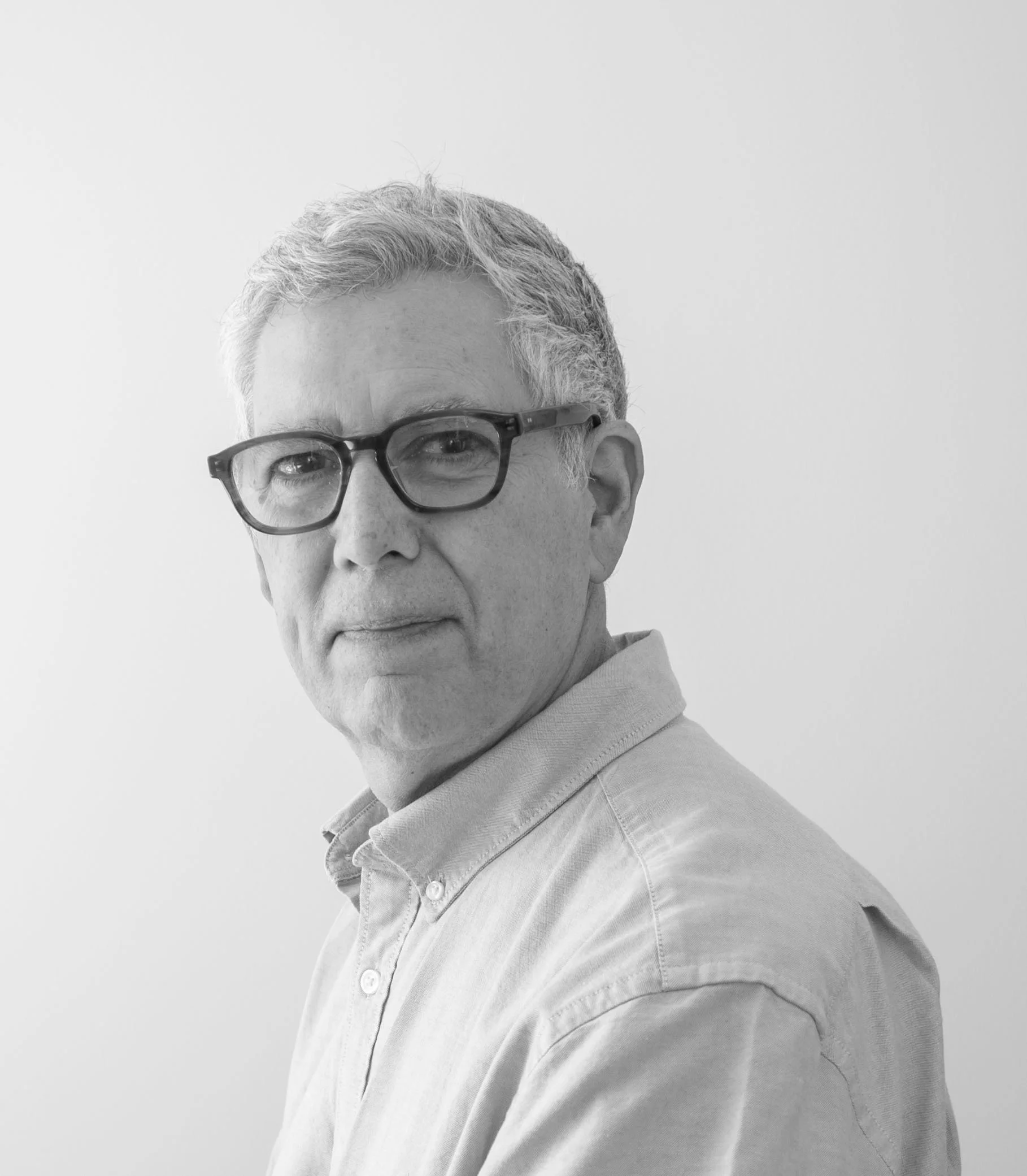 Black and white portrait of a middle-aged man with glasses, wearing a button-down shirt, looking at the camera against a plain background.