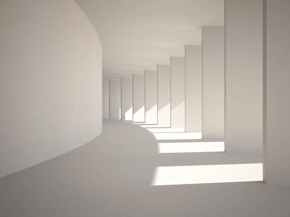 A minimalist architectural space with curved and straight white walls, large rectangular windows, and sunlight casting shadows on the floor.