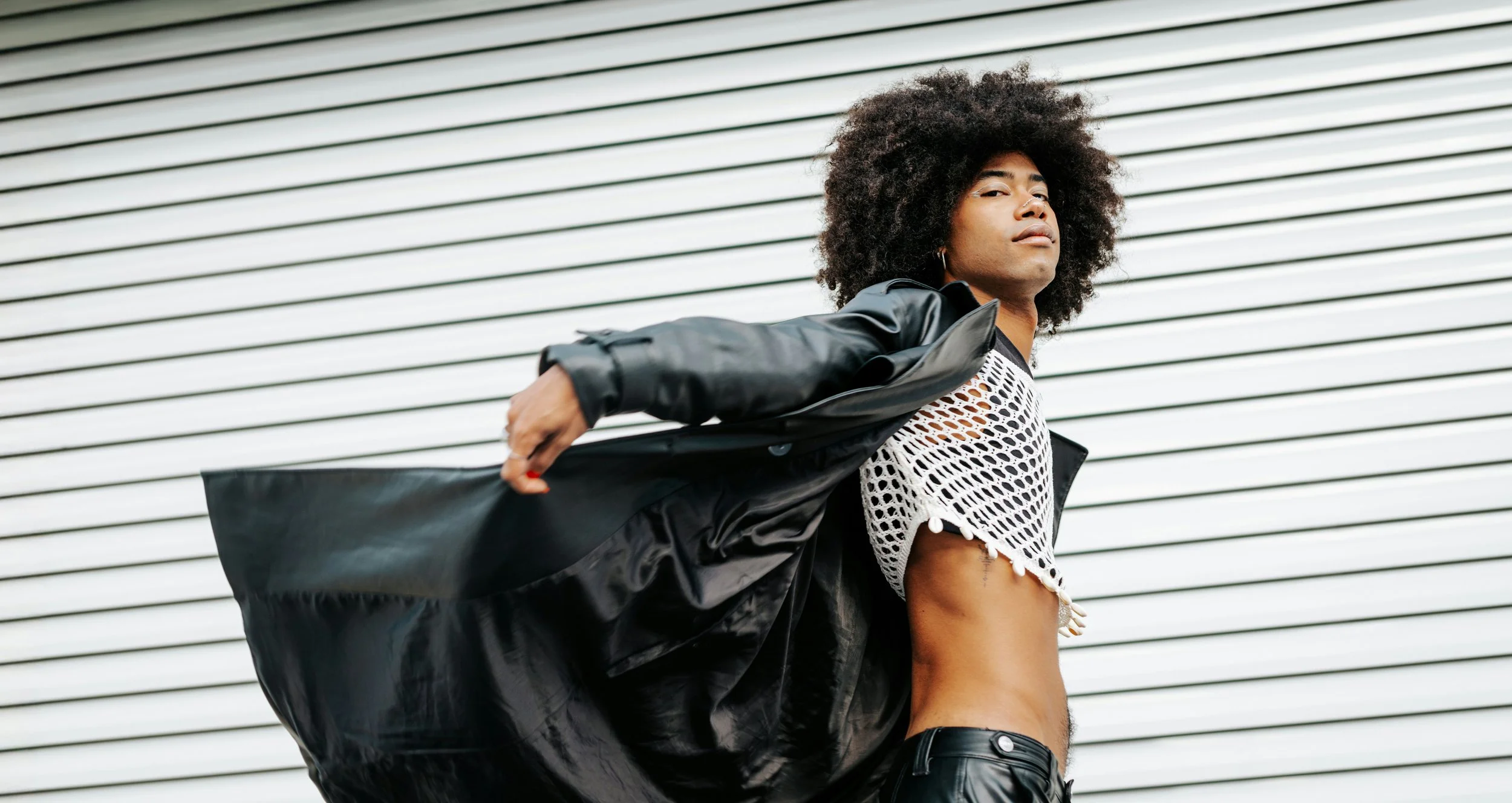 Fashionably dressed man with an afro hairstyle striking a confident pose against a striped background.