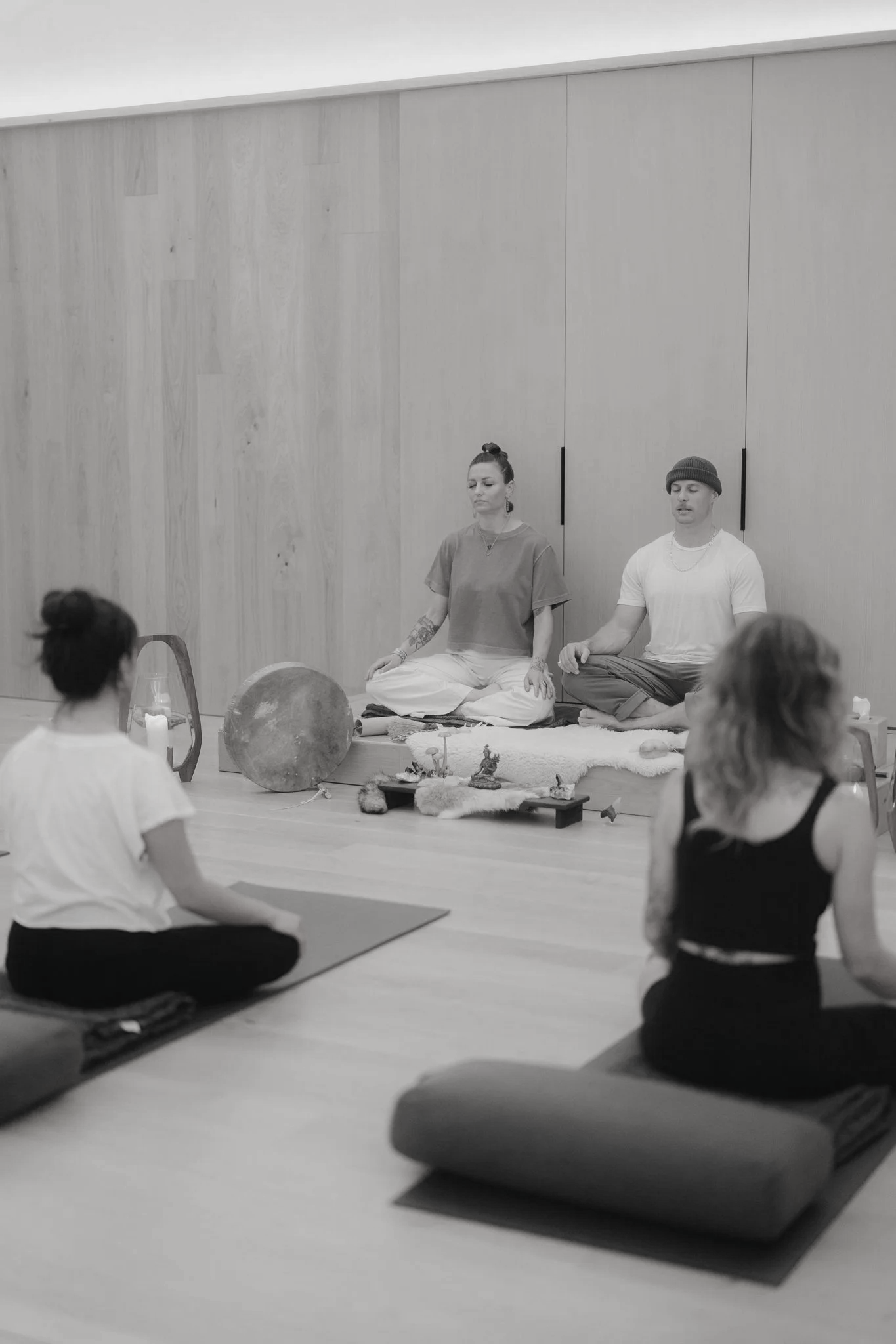 People participating in a breathwork session in a minimalist room with wooden walls, seated on mats with meditation objects in front.