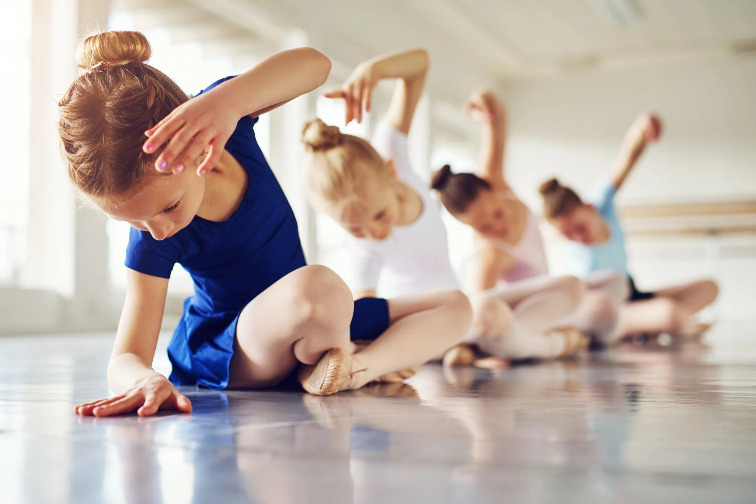 Children in ballet class stretching on the floor.