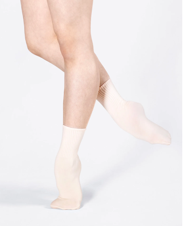 Close-up of a person wearing white knee-high compression socks, standing with one leg bent and foot raised.