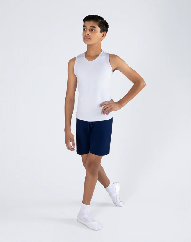 Young boy standing in a relaxed pose, wearing a white sleeveless shirt, dark blue shorts, white socks, and white shoes against a plain light background.