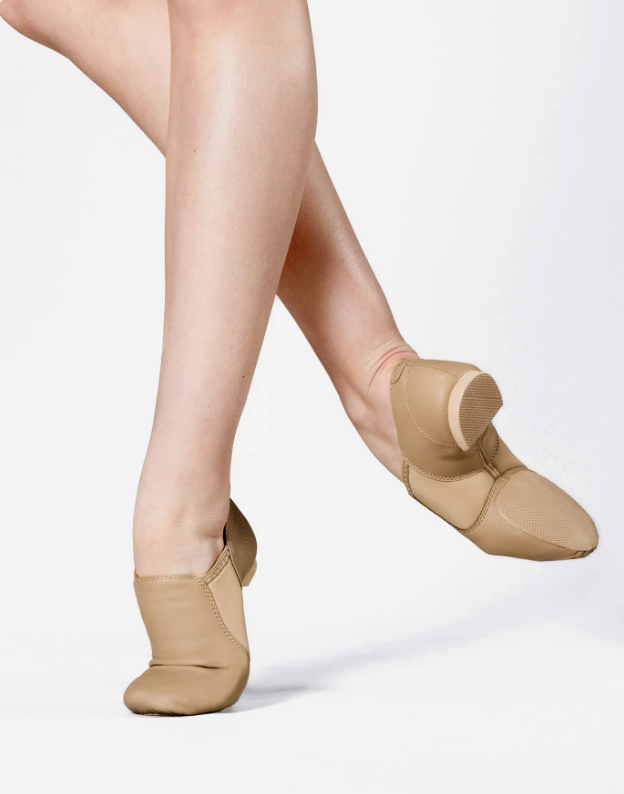 Close-up of a person's legs and feet wearing beige dance slippers, standing on a white background.