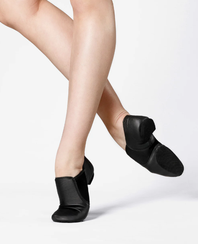 Close-up of a person's legs and feet wearing black ballet slippers on a white background.