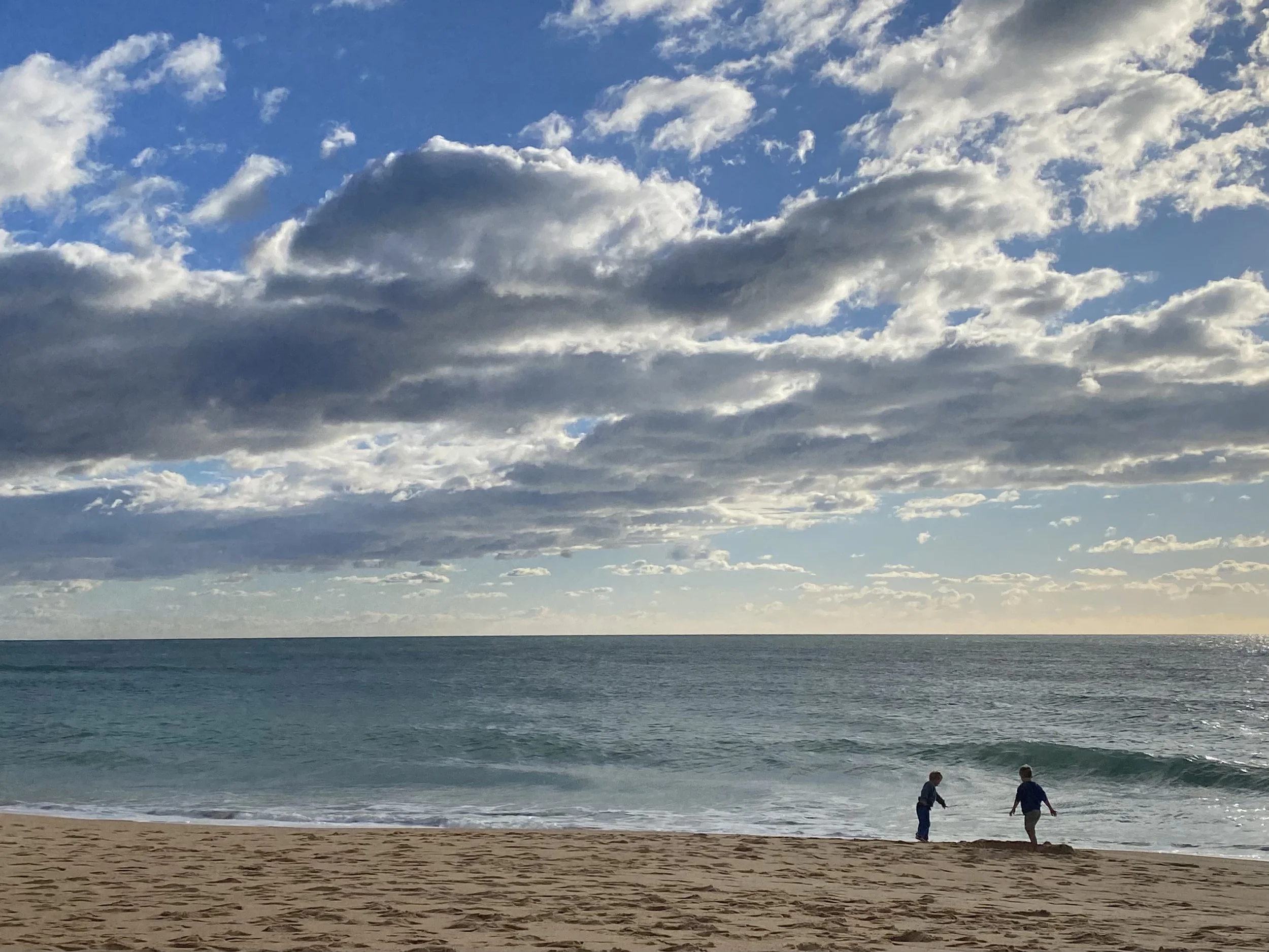 Two children playing on a sandy beach with ocean waves and a cloudy sky.