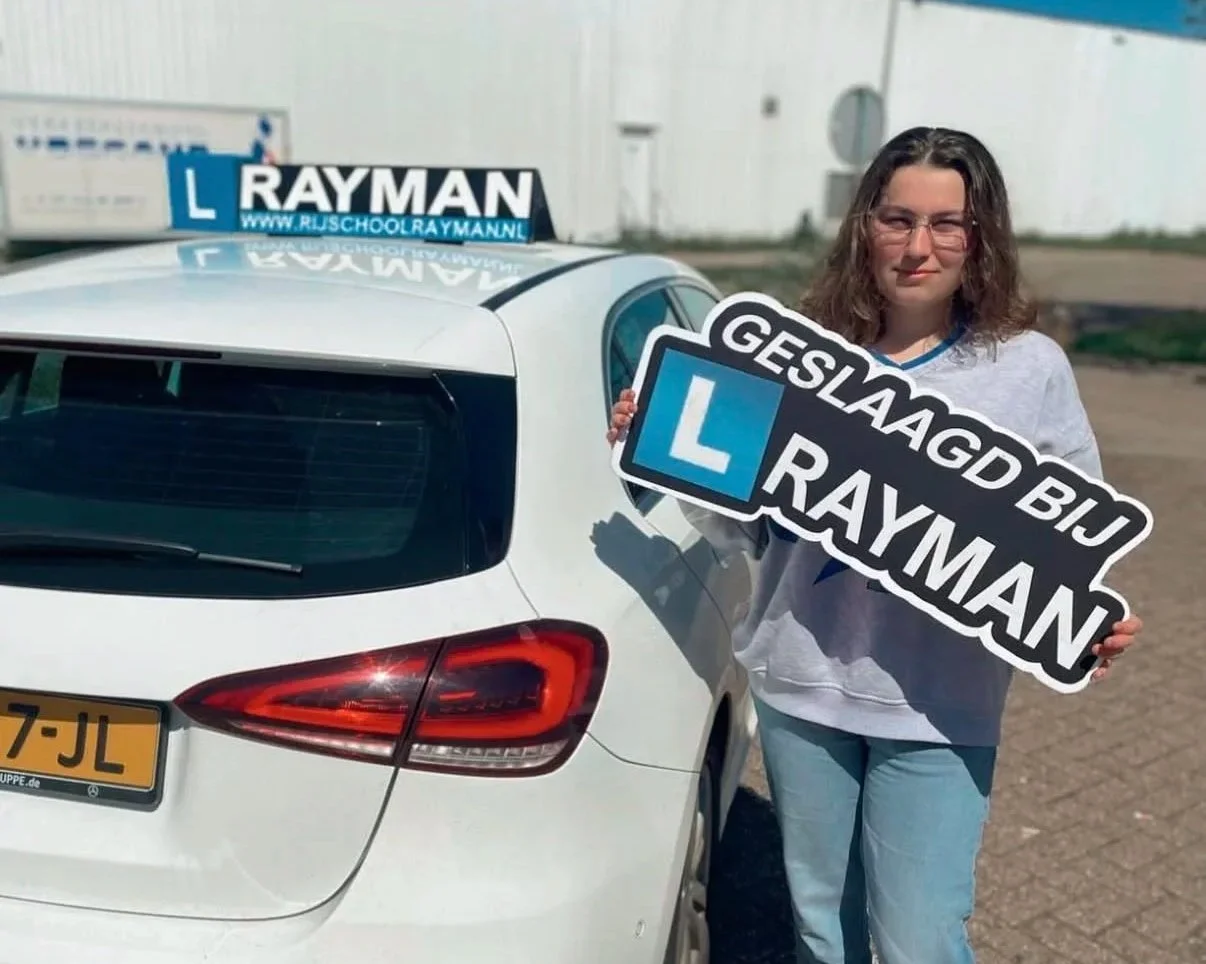 Vrouw met rijbewijs gehaald bord naast witte auto op parkeerplaats.