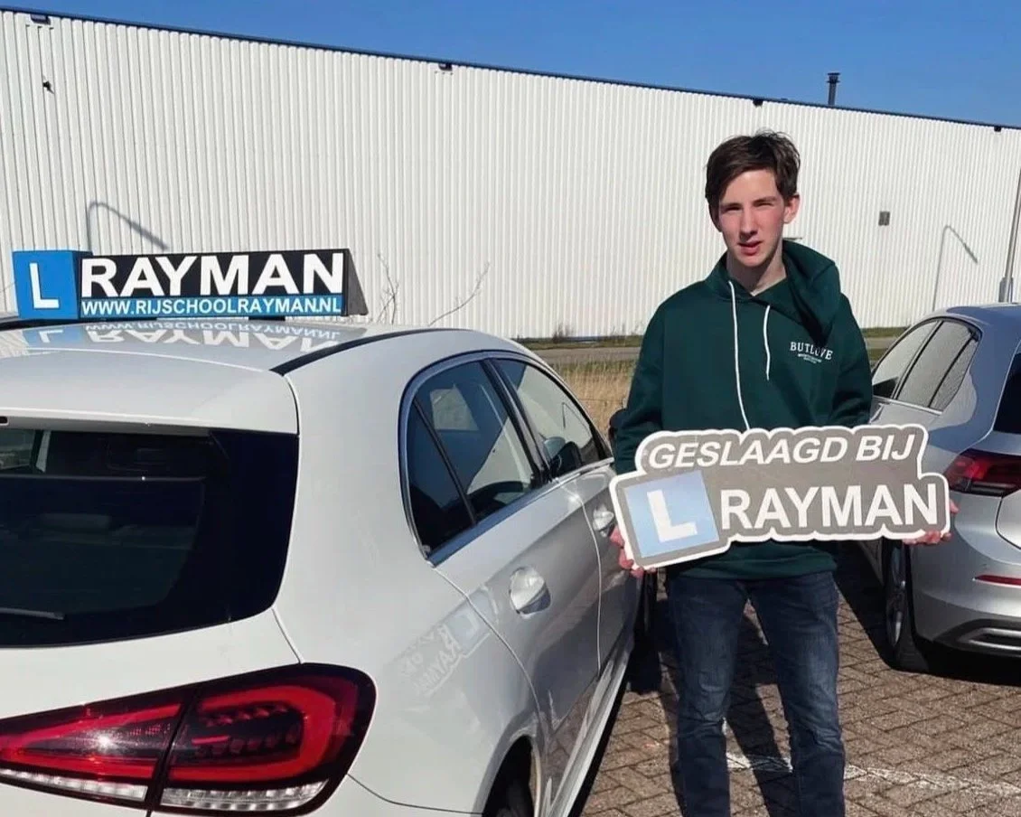 Jongen die trots voor CBR examenlocatie in Deventer staat met bord geslaagd bij Rayman, deze jongen is geslaagd bij rijschool Rayman uit Terwolde