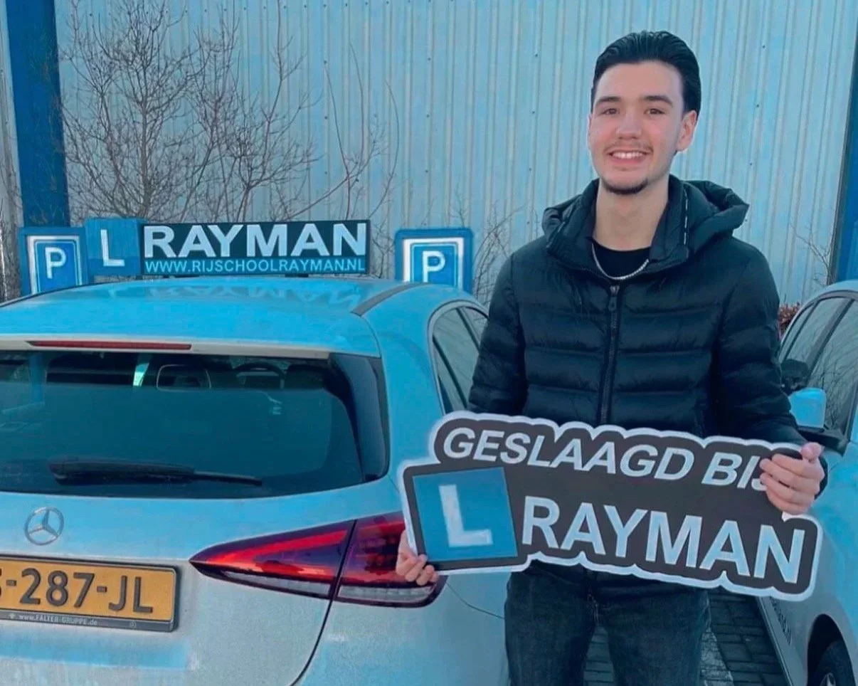 Een jongeman uit Twello die geslaagd is en een bord vasthoudt met geslaagd bij Rayman, een autorijschool uit Terwolde die rijlessen geeft in omgeving Deventer. 