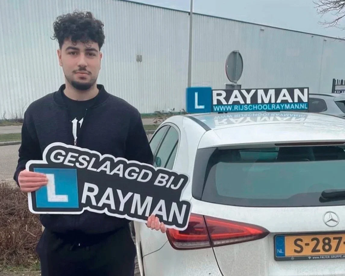 Jongeman uit deventer die na zijn autorijlessen trots is dat die is geslaagd, deze leerling houdt een bord vast met geslaagd bij Rayman
