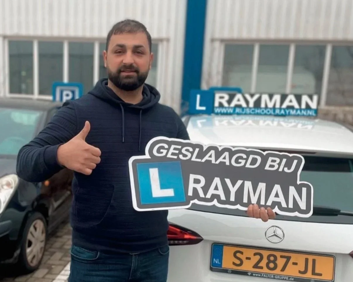 Man met een duim omhoog die een bord vasthoudt met 'GELBAGD BIJ RAYMAN' en een auto met een Leerautorijbewijs en meerdere 'L' verkeersborden op het dak.