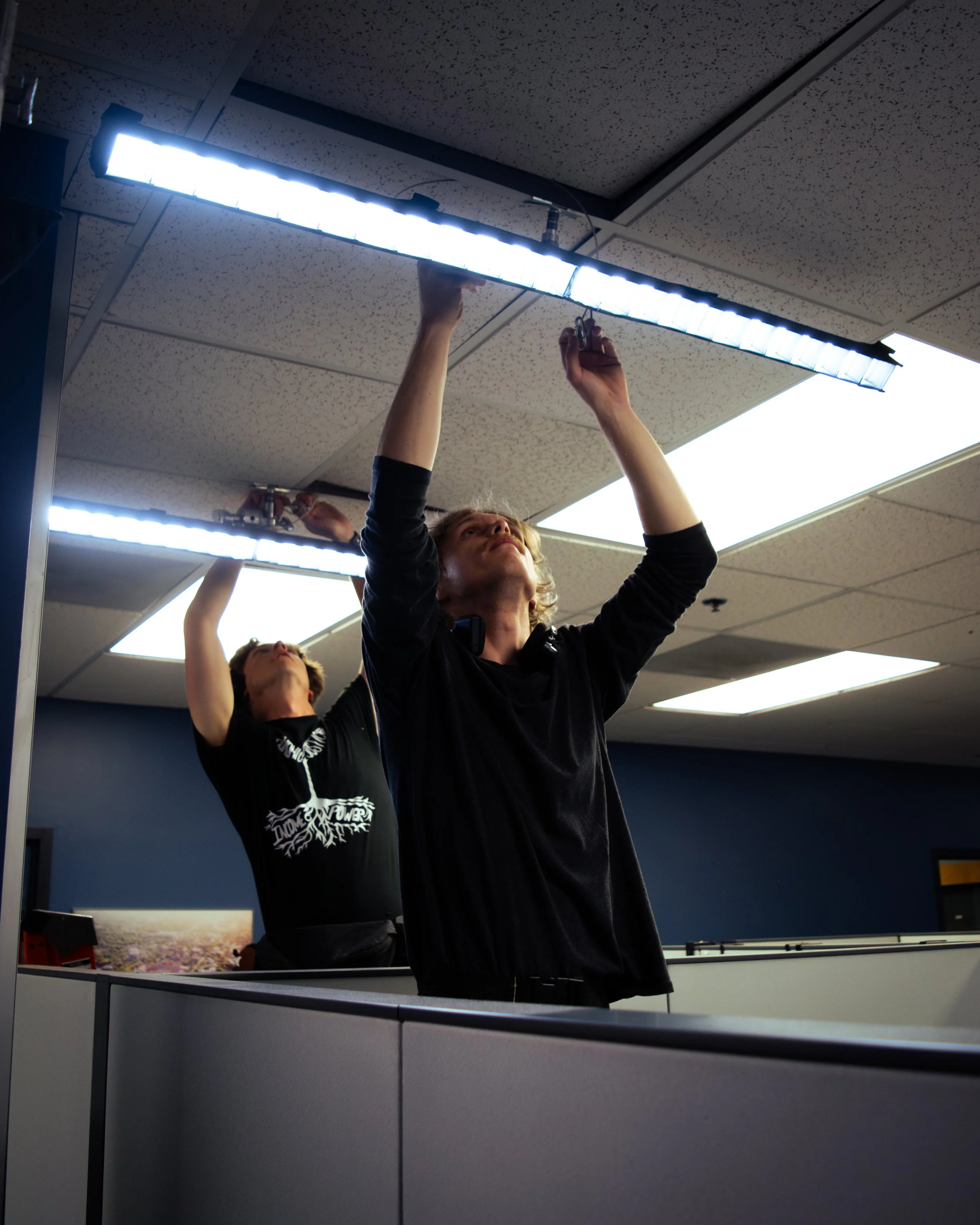 Two men installing LED lighting on office ceiling.