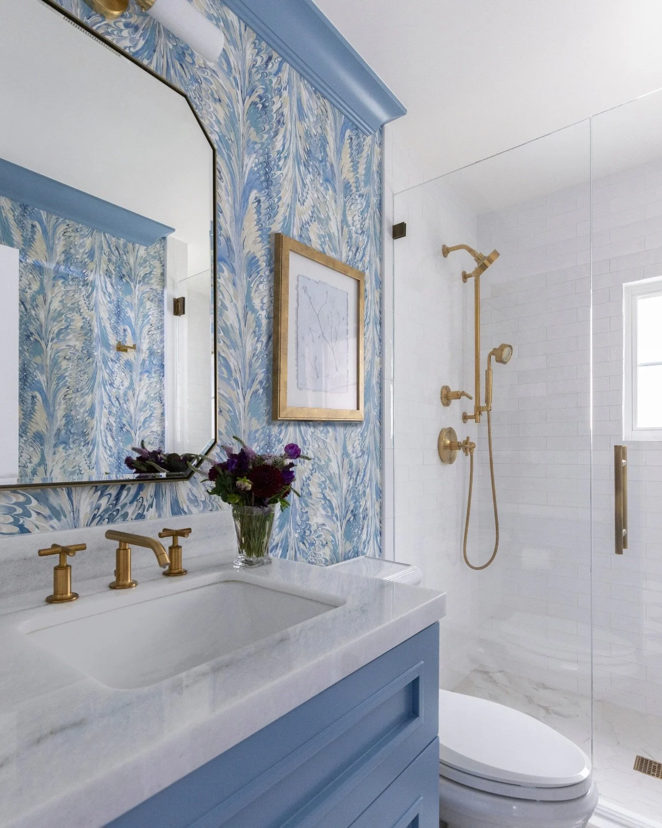 This bathroom is a perfect example of how color can completely set the tone of a space. We leaned into soft blues to keep things calm and timeless, then layered in warmth with the brass fixtures to give it that little glow.

The wallpaper adds moveme