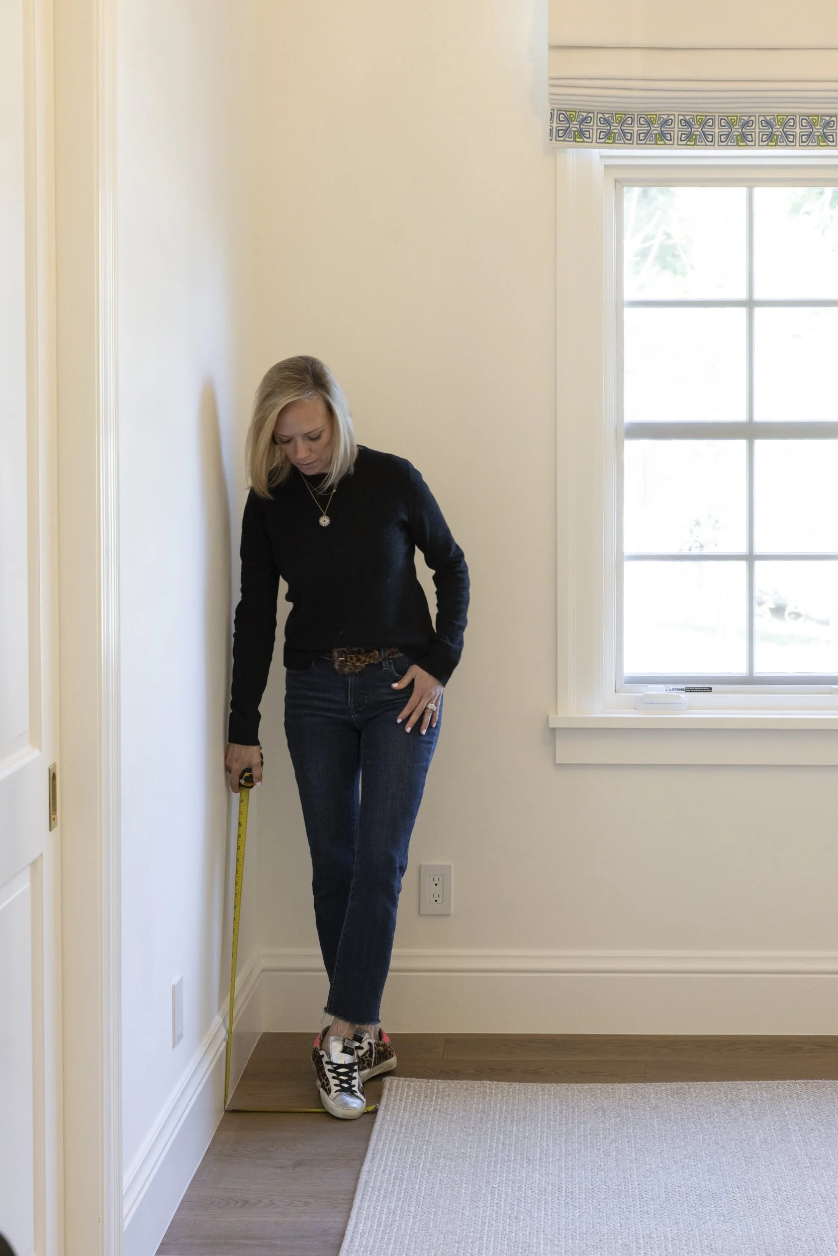 Woman measuring the height of a wall in a room with a tape measure.