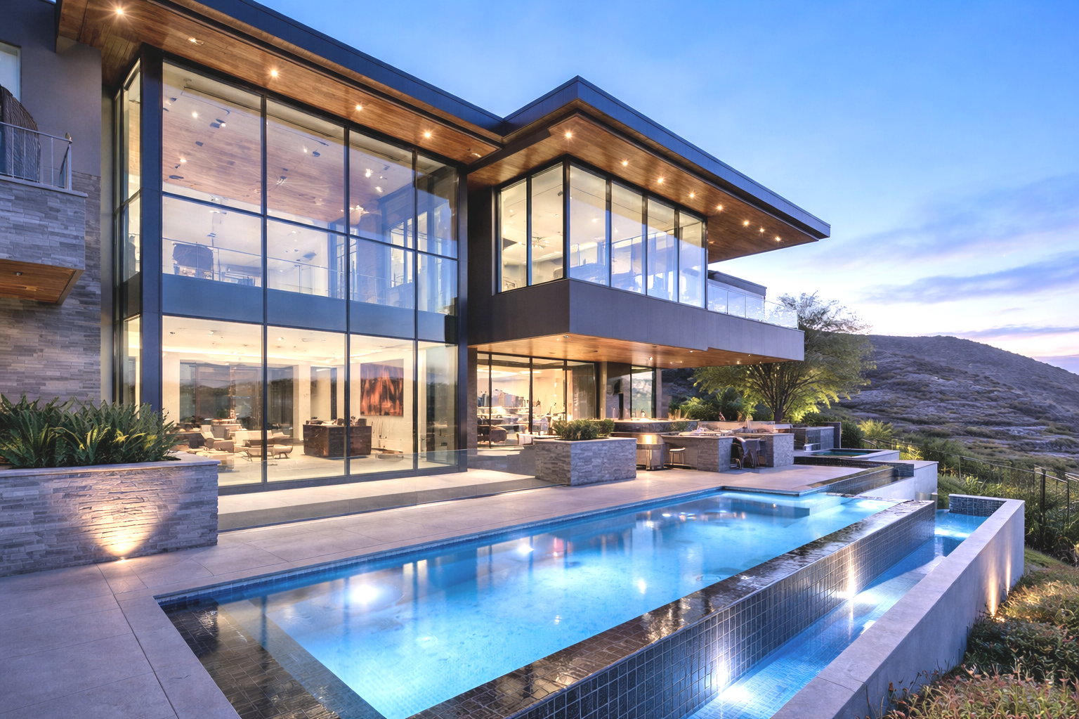Modern multi-story house with large glass windows, outdoor pool, and mountain view at dusk, warm interior lighting visible through windows.