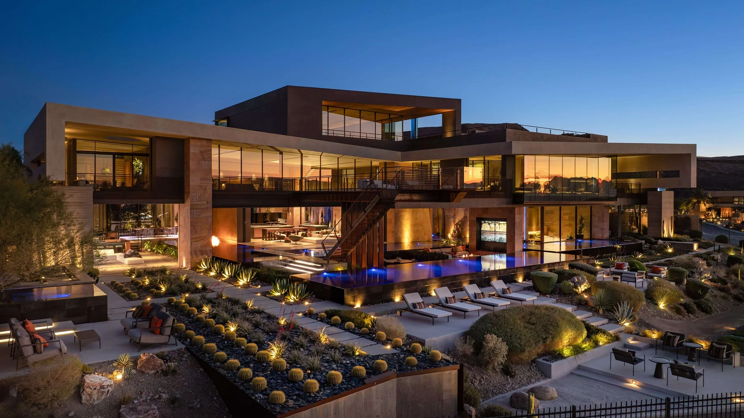 Luxury modern house with large glass windows, outdoor lighting, swimming pool, and landscaped yard at dusk.