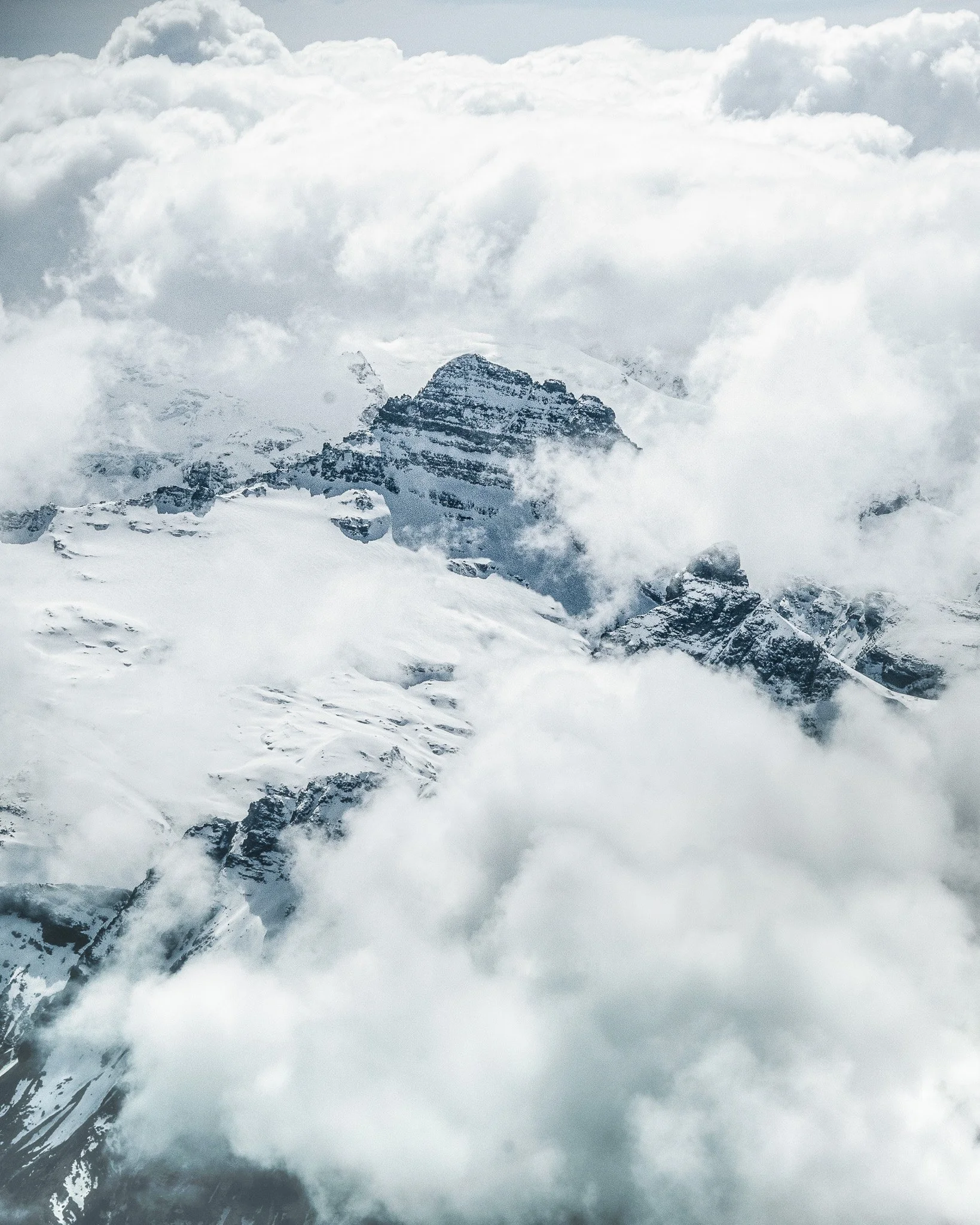 Snow-covered mountain peaks with clouds surrounding them.